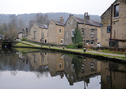 houses alongside the rochdale canal in hebden bridge with reflections in the water and lock gates in the distance