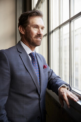 Fototapeta premium Senior white businessman looking out of window, vertical