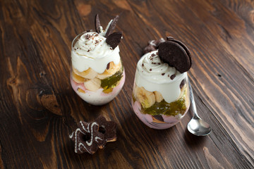 Dessert in a glass with a banana, biscuits and jelly on a wooden table