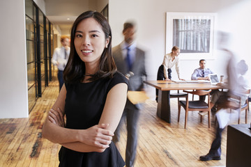 Fototapeta premium Portrait of young Asian woman in a busy modern workplace
