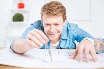 Easy task. Cheerful clever experienced engineer coping with an easy task while holding a pair of compasses and measuring the distance on his drawing