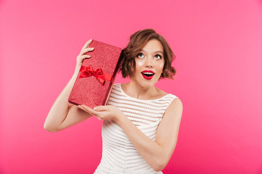 Portrait of a cheery girl dressed in dress holding gift