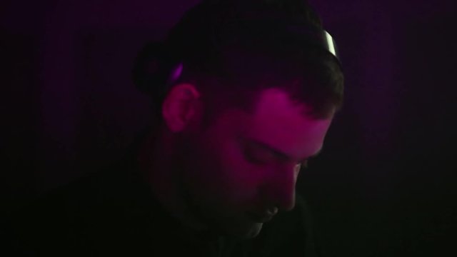 closeup of a DJ puts headphones on his head and plays music using the music pane. The crane moves the camera vertically.