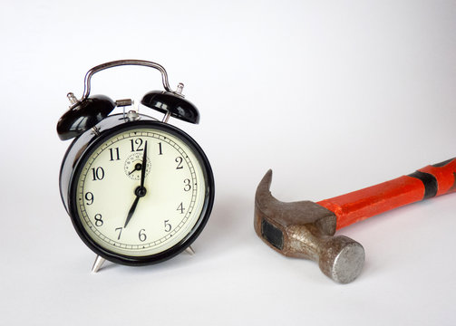 alarm clock and hammer are on the table. white background. the beginning of the morning.
