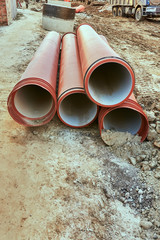 Red underground pipes lie on the ground before laying