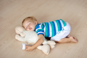 Baby sleeping on floor with toy and milk bottle.