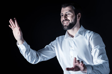 Virtual technology. Positive cheerful nice man looking at the invisible screen and smiling while using virtual technology