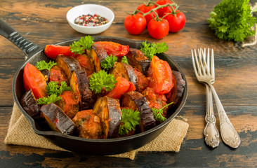 Turkish traditional dish kebab with eggplant, tomatoes and fresh parsley in black pan on rustic wooden table.