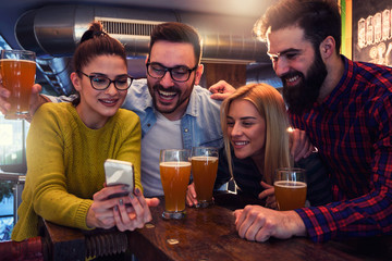 Friends in Pub drinking Beer and Looking at Smartphone