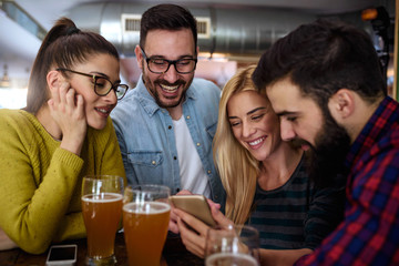 Friends in Pub drinking Beer and Looking at Smartphone