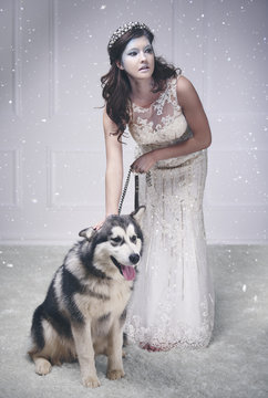Pretty ice queen with dog among snow falling