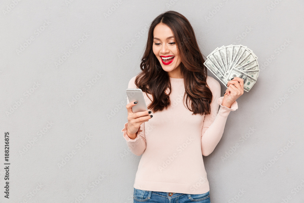 Poster portrait of attractive brunette female 30s winning lots of money dollar currency using her smartphon