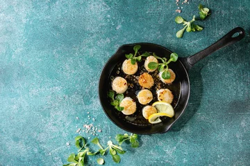 Deurstickers Fried scallops with butter lemon spicy sauce in cast-iron pan served with green salad over turquoise texture background. Top view, copy space © Natasha Breen