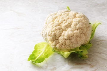 Cauliflower, whole head, healthy vegetable on a light kitchen marble plate, copy space, selected focus