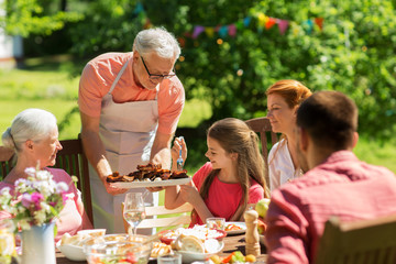 family having dinner or barbecue at summer garden