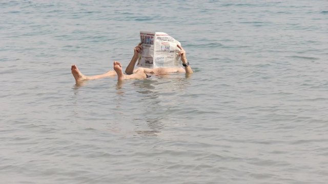 a man floats in the incredibly salty dead sea of israel and reads a newspaper
