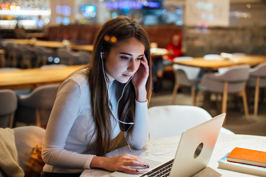 Attractive and pretty young professional woman, does freelance work, works out of office in cafe at night time or evening. Vintage look and feel. Small earphones connected to laptop. Future concept