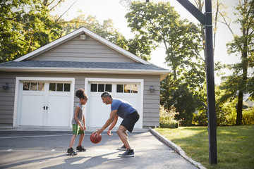 Father And Son Playing Basketball On Driveway At Home