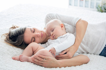 Mother and her baby son, sleeping on a big bed, soft back light