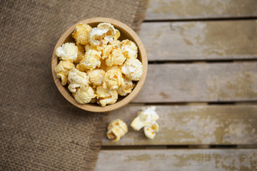 Salted popcorn in round wooden bowl on old wooden table 