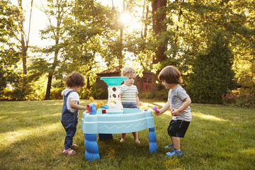 Group Of Young Children Playing With Water Table In Garden