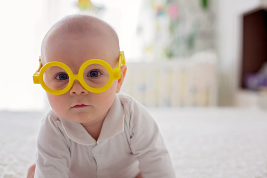 Little baby boy, toddler, playing at home with funny eye glasses in bed
