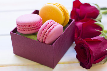 The concept of Love, Wedding, Proposal, Anniversary, St. Valentine's Day, Mother's Day with beautiful red velvet roses and a box of macaroons in a close up, light wooden background