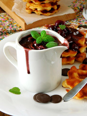 Cherry and chocolate sauce served in the white gravy boat with waffles