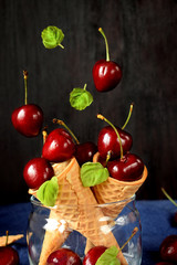 Cherries falling into waffle cones on dark wooden background. Ingredients for a summer dessert cooking
