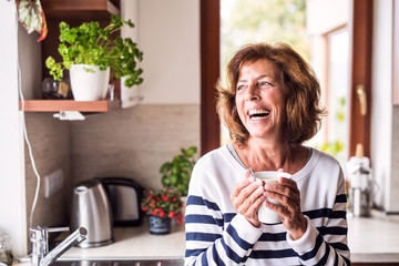 Senior woman holding a cup of coffee in the kitchen. - Powered by Adobe