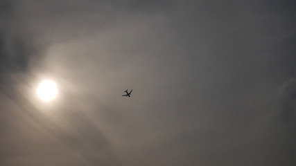 The Sun and Silhouette of an Airplane Flying in Cloudy Sky