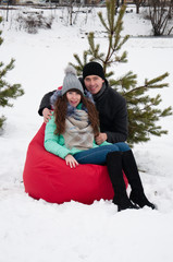 Obraz premium A couple, a man and woman are sitting in a red armchair against the background of a snow-covered, winter park