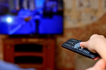 The man with the remote control in hand watching the sports channel and presses the button on the...