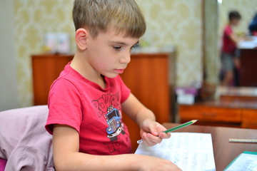 A child of primary school age do homework. The boy does his homework at his desk at home. The student / pupil has been bored on the lesson. Boy fell asleep during homework. Lovely first grader.