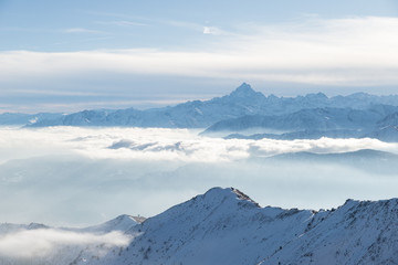 Snow mountains in backlight, bright sunny day winter on the Alps, high snowcapped mountain peaks, fog and clouds in the valleys below.