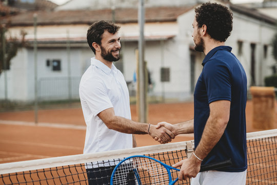 Two young men handshake after a tennis match on a clay court
