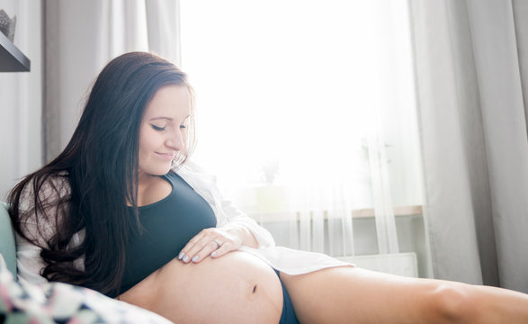 Relaxed smiling pregnant woman lying on sofa resting at home