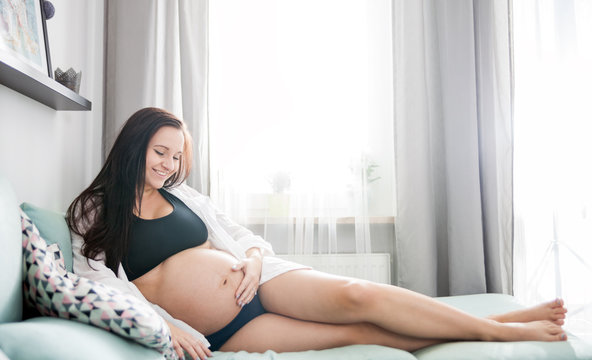 Relaxed smiling pregnant woman lying on sofa resting at home