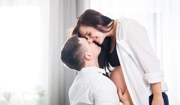 Pregnant couple hugging and kissing at home expecting baby