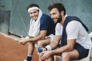 Two young men having a break after a tennis match on a clay court