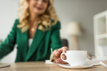 close-up partial view of businesswoman holding cup of coffee at workplace