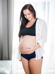 Beautiful pregnant woman standing near window at home