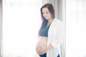 Beautiful pregnant woman standing near window at home