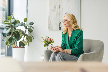 smiling businesswoman in eyeglasses holding smartphone and looking away