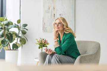 pensive businesswoman in eyeglasses holding smartphone and looking away