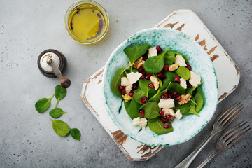 Fresh useful vegetarian wholesome spinach, pomegranate seeds, walnut, saffron, pepper and ricotta salad on  gray  background. Selective focus. Top view. Copy space for text.