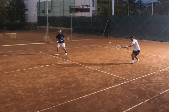 Group of friends play tennis a double match on a clay court