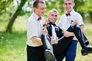 Two groomsmen holding groom and having fun next to the castle.