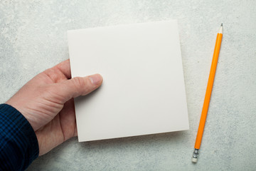 An empty square piece of paper in a man's hand, a yellow pencil next to it. Mock-up.