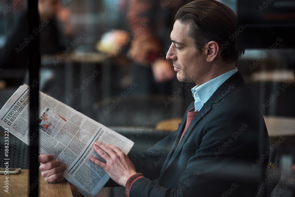 Poster side view serious male looking through article while locating at table in cafe. information and rest